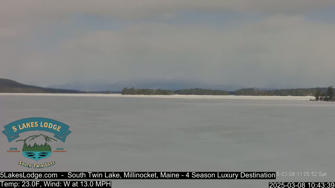 A mostly frozen lake is visible, with a distant, snow-dusted shoreline and overcast skies.