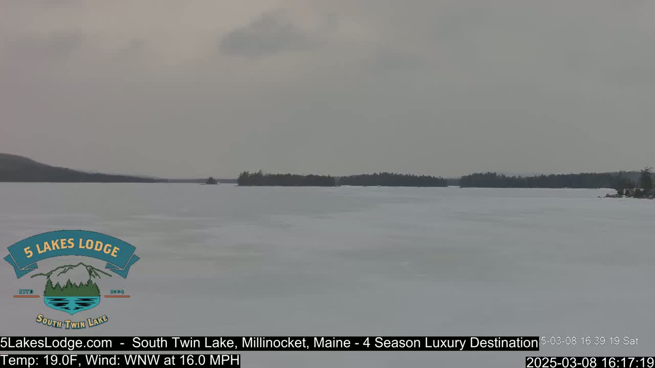 A frozen lake stretches to a treeline under an overcast sky.