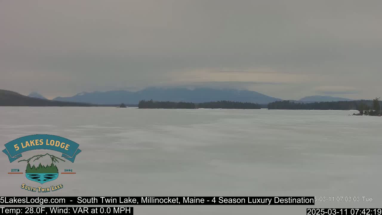 A frozen lake stretches out to distant, low mountains under a cloudy, gray sky.
