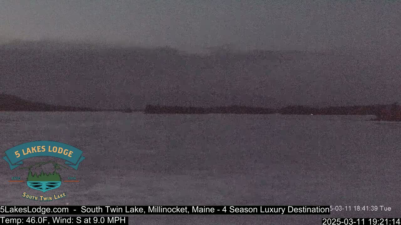 A dark, overcast view of a lake with distant, indistinct hills under a gray sky.