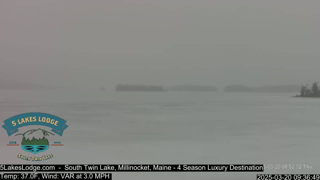 A hazy, snowy scene shows a body of water with indistinct landmasses in the distance.