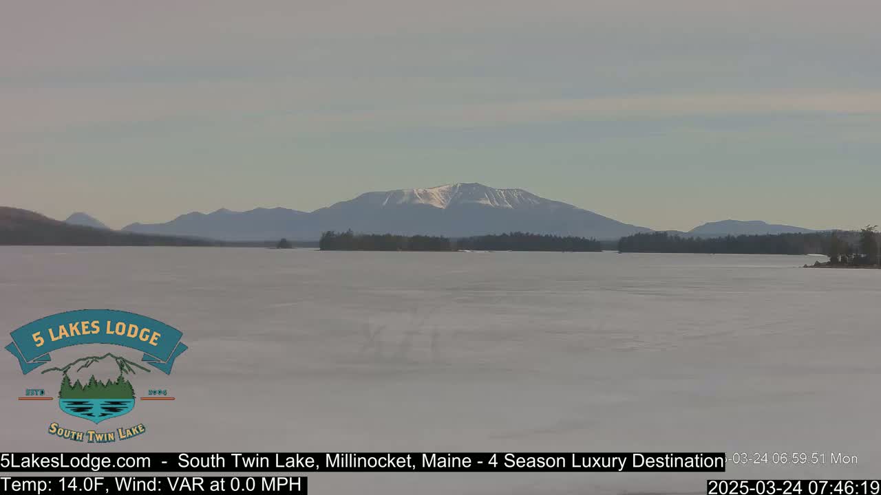 A frozen lake stretches toward snow-capped mountains under a pale sky.