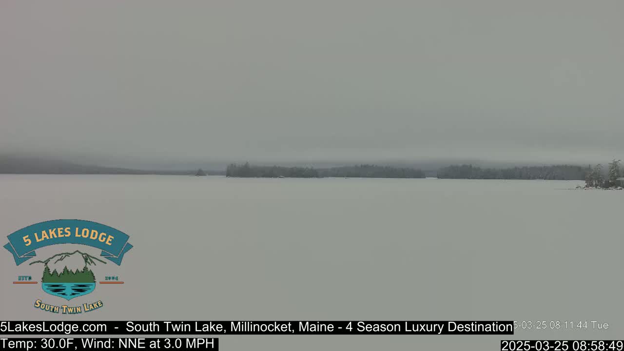 A snow-covered lake stretches to a distant, hazy treeline under an overcast sky.