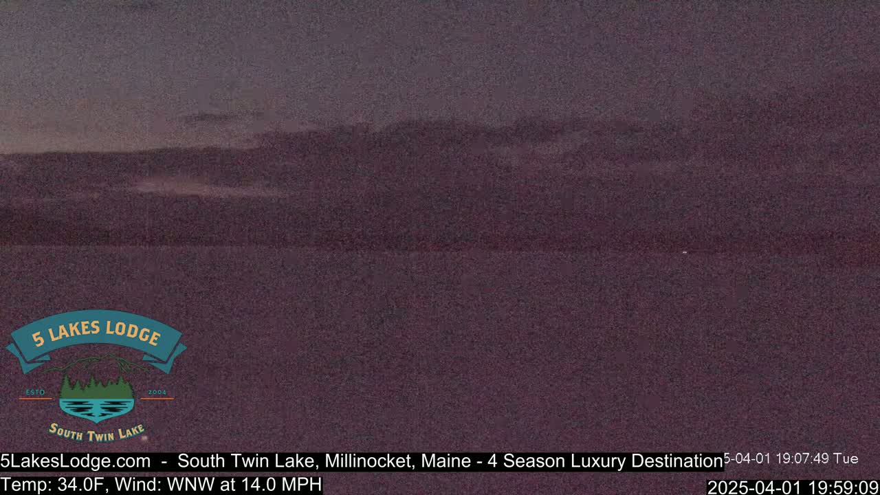 A dark, twilight view of a lake and distant hills under a mostly clear sky.