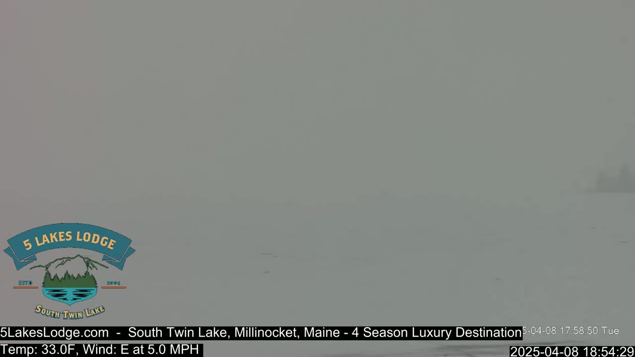 A hazy, snowy scene shows a flat expanse of land with a few indistinct objects in the distance.