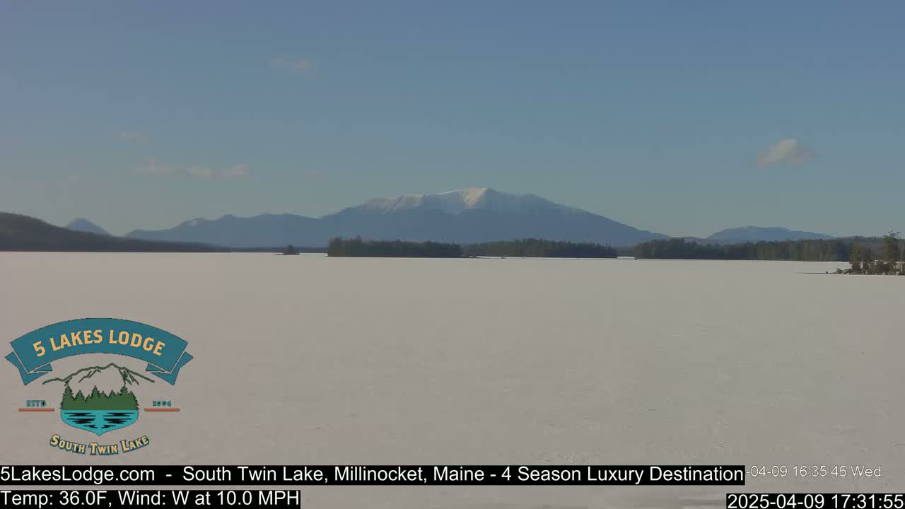 A snow-covered lake stretches to a distant mountain range under a clear blue sky.