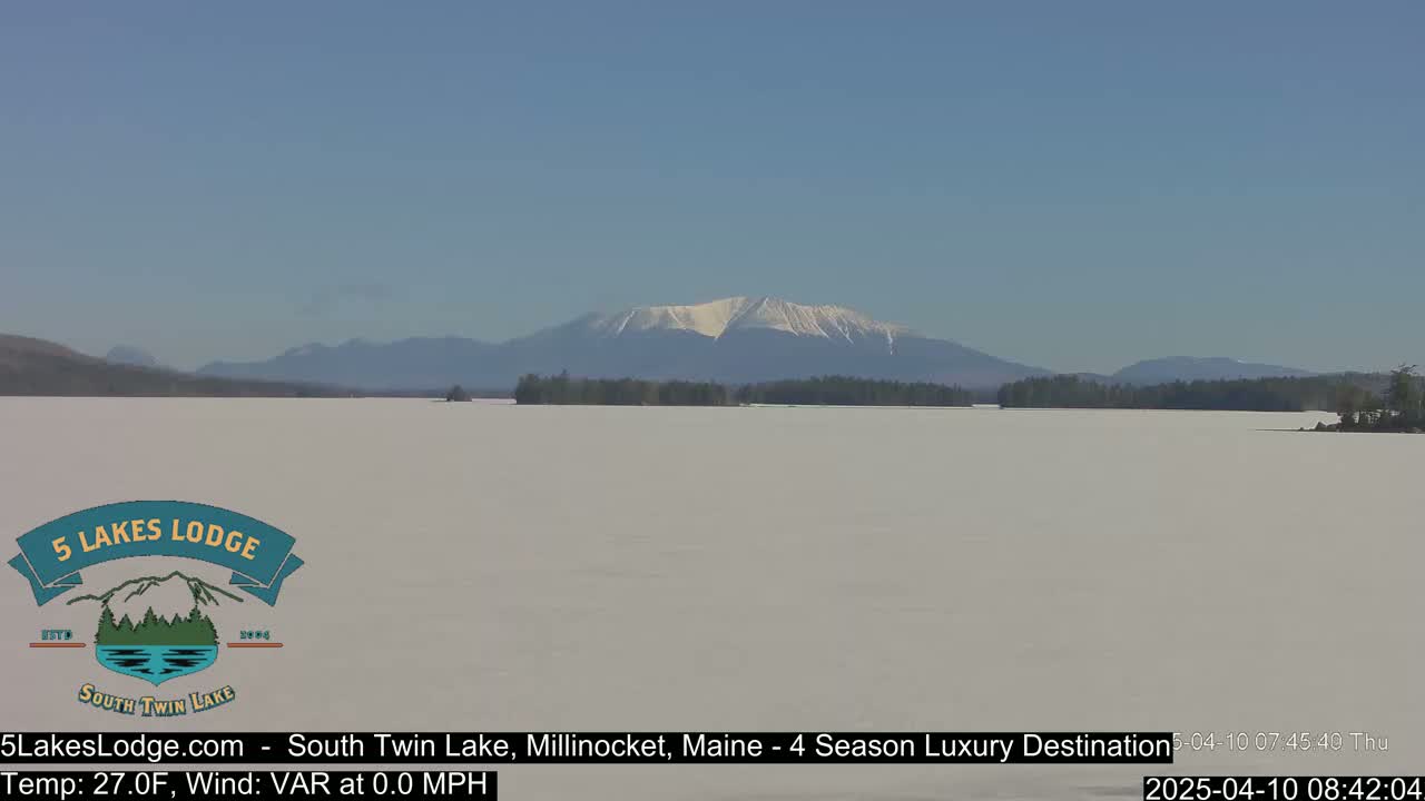 A snow-covered lake stretches to a distant mountain range under a clear blue sky.