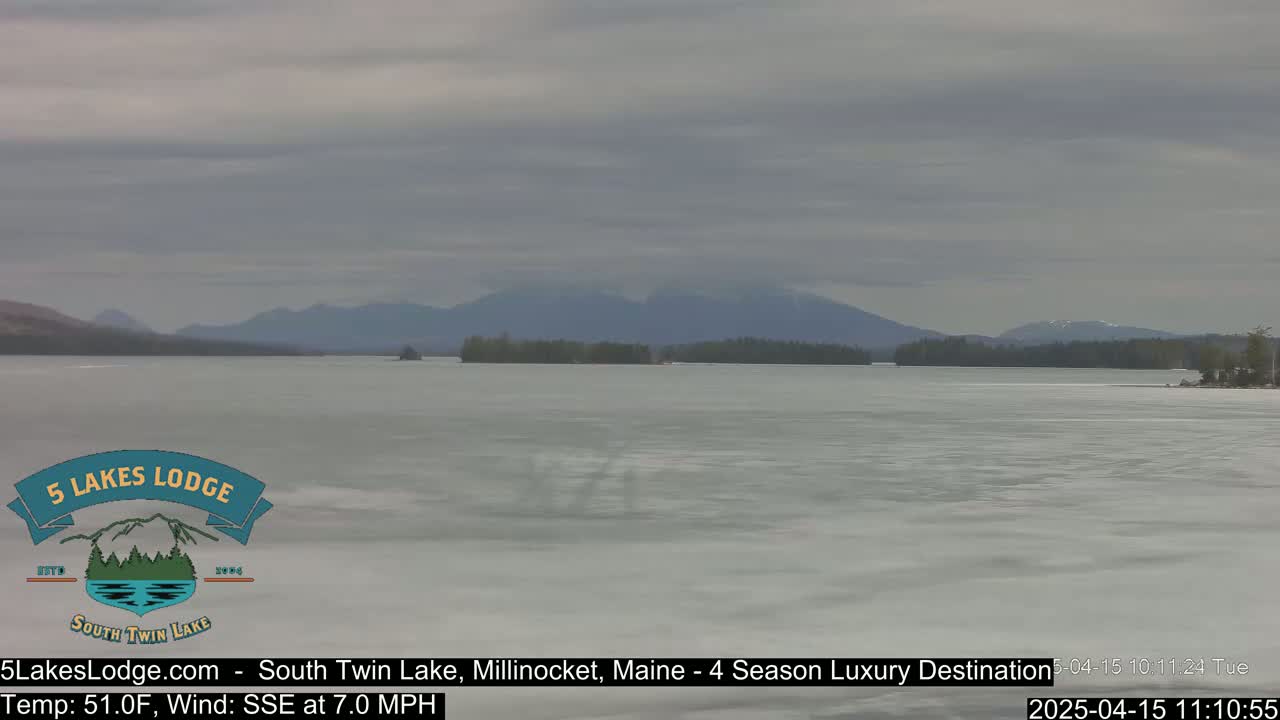 A mostly frozen lake with distant mountains under an overcast sky, with a light wind blowing from the south-southeast.