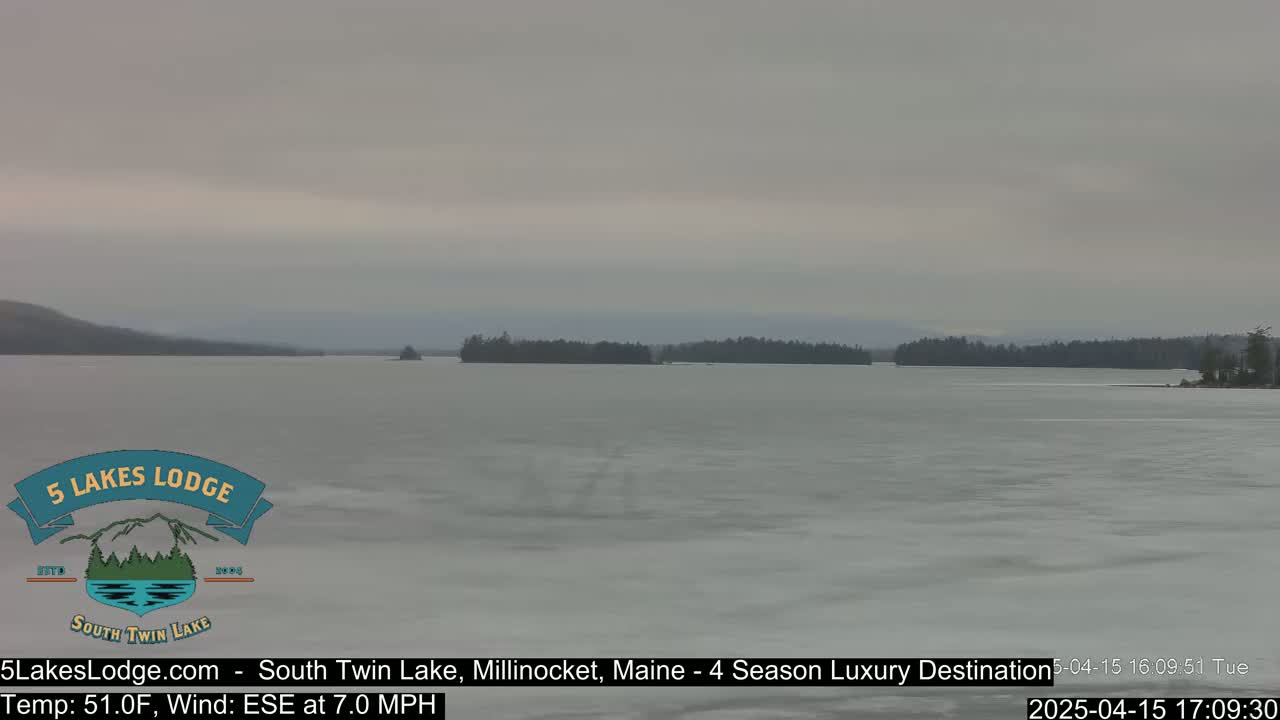 A mostly frozen lake stretches to the horizon under an overcast sky, with dark tree lines visible on both shores.