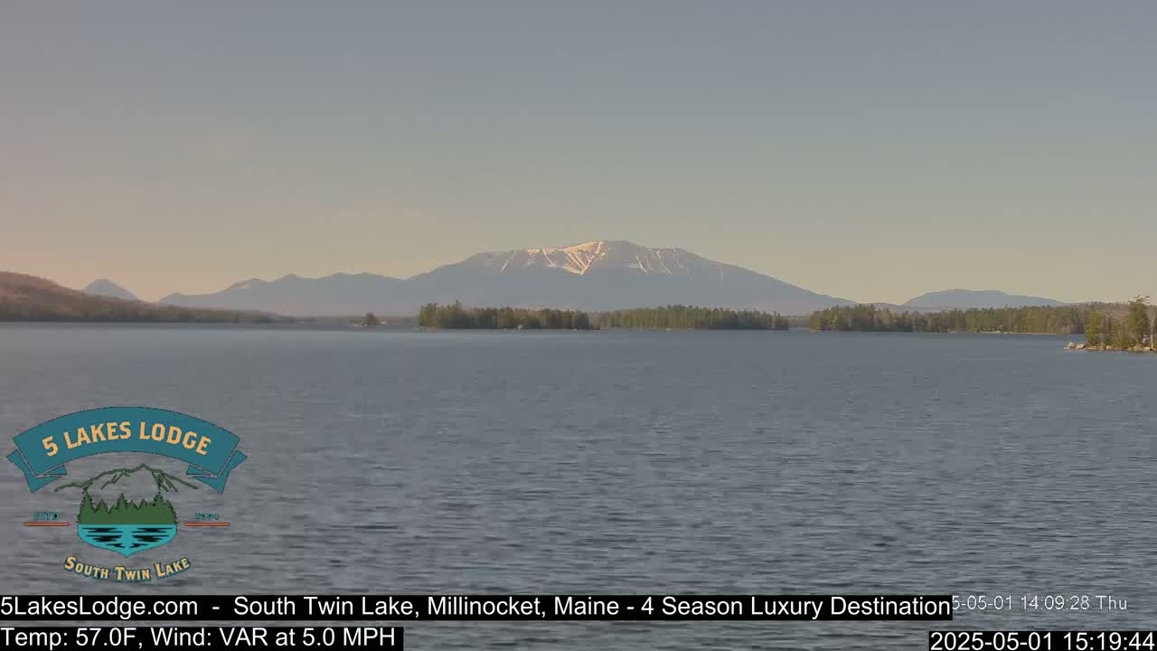 A calm lake with a distant mountain range showing some snow under a clear, pale sky.