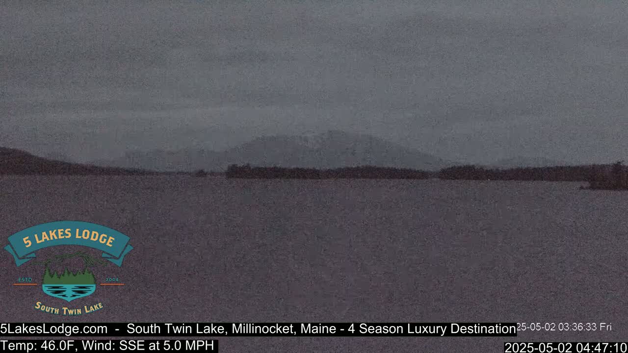 A calm, overcast body of water is shown with a dark mountain range in the background.