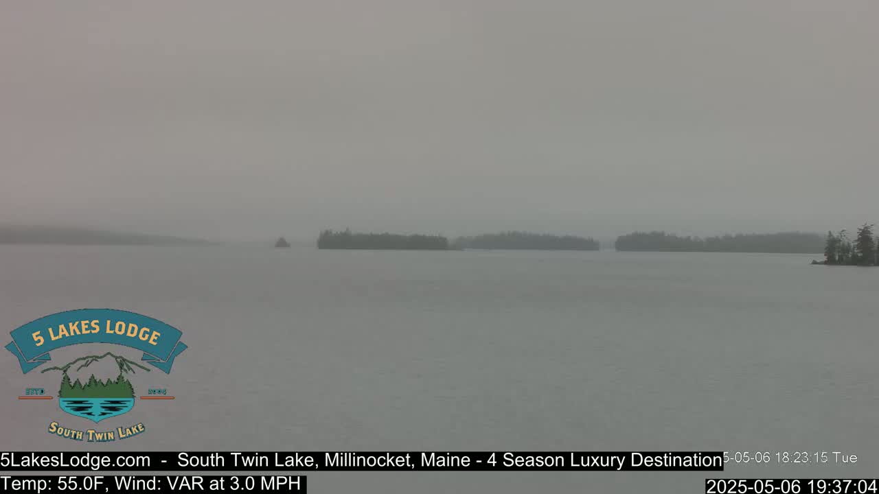 A hazy, overcast view shows a calm lake with dark tree-lined shorelines and small islands in the distance.