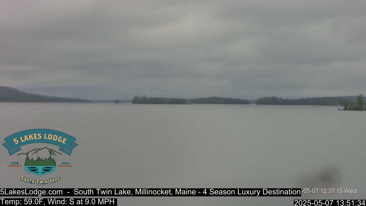 A calm lake stretches to a tree-lined shore under an overcast sky.
