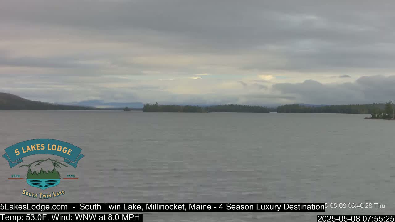 A calm lake stretches to a tree-lined shore under an overcast sky.