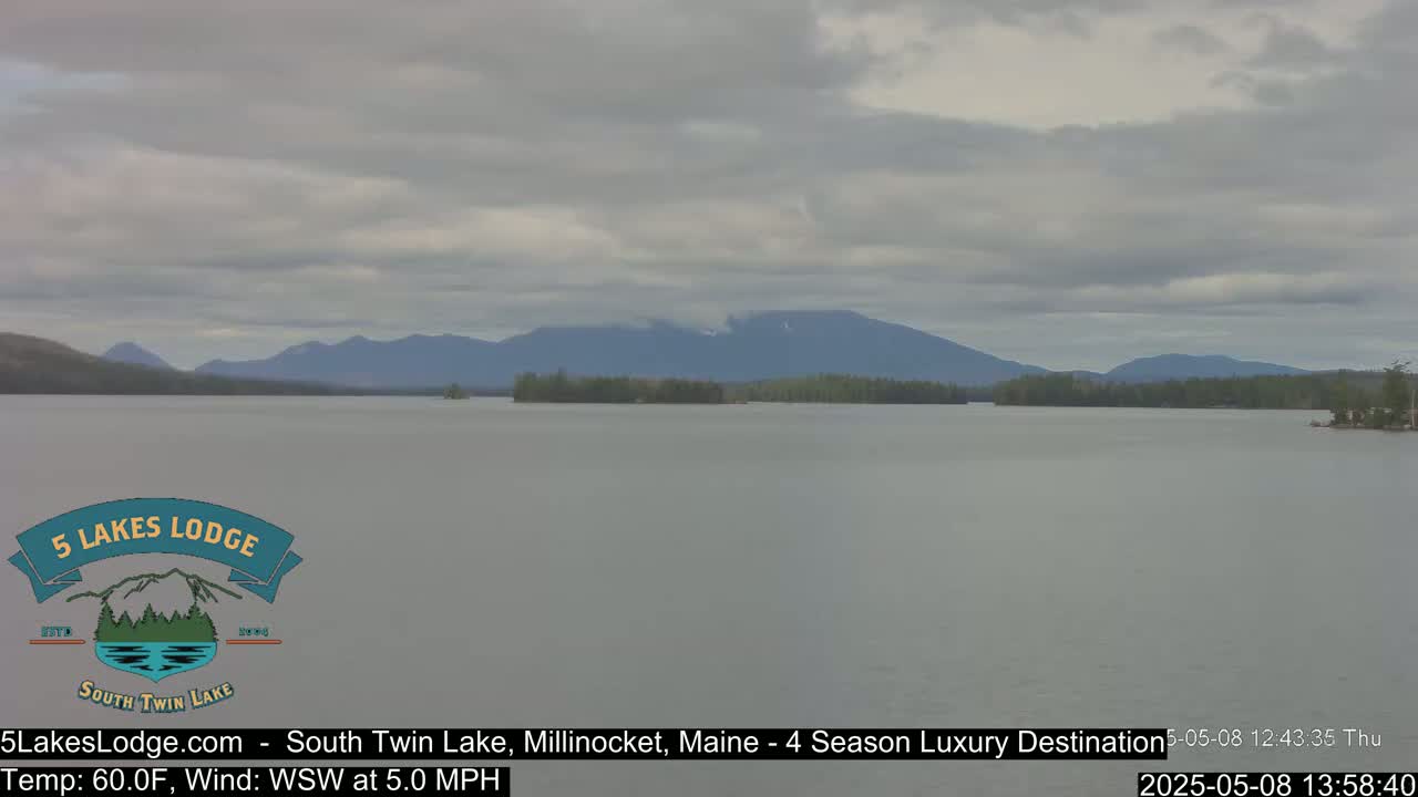 A calm lake with a distant mountain range under a cloudy sky.