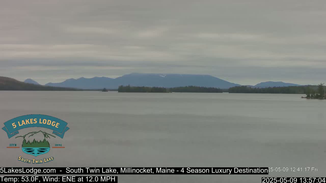 A calm lake stretches out to a range of distant mountains under an overcast sky.