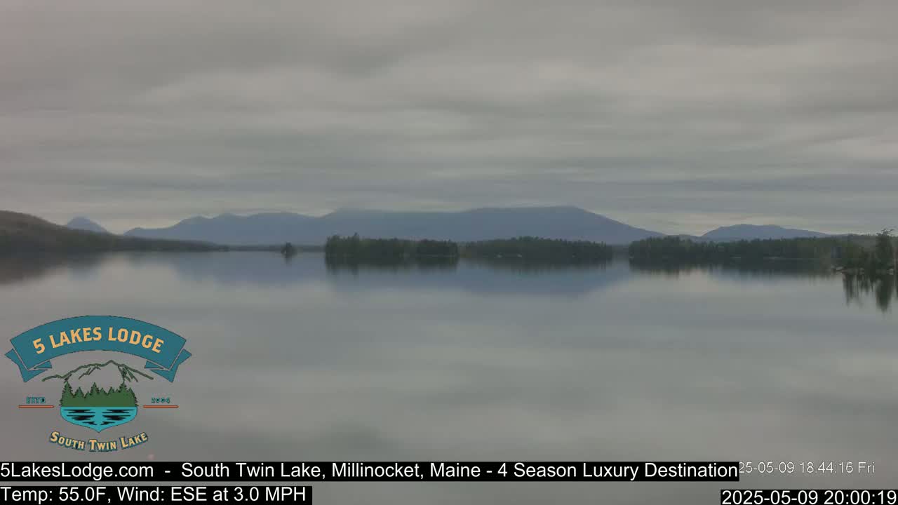 A calm lake reflects a hazy sky and distant mountains under overcast conditions.