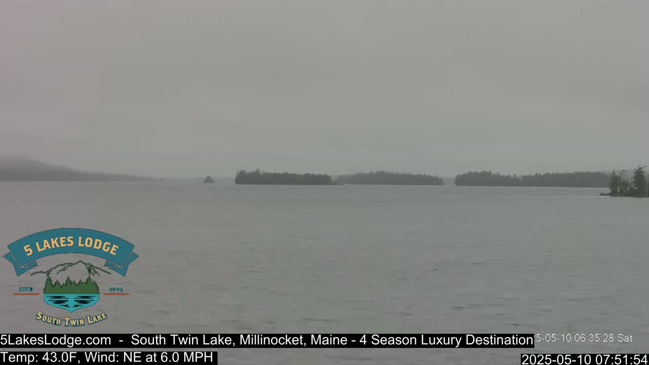 A calm lake is shown under an overcast sky, with small forested islands in the distance.