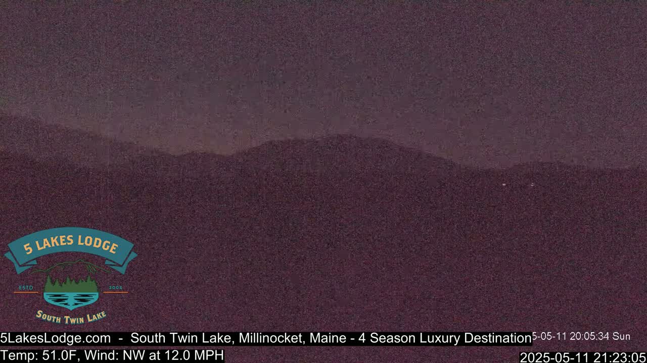 A dark, nighttime view of distant mountains under a mostly clear sky, with a northwest wind at 12 mph and a temperature of 51°F.