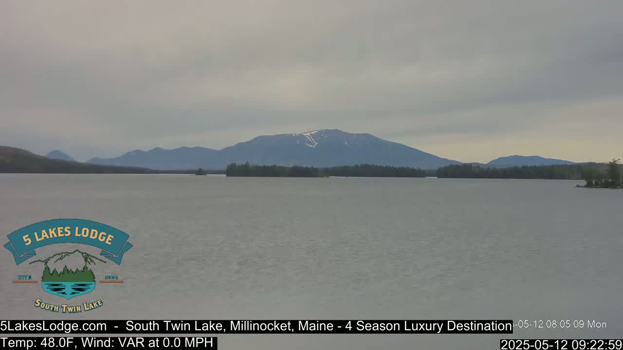 A calm lake stretches out before a range of mountains under an overcast sky.