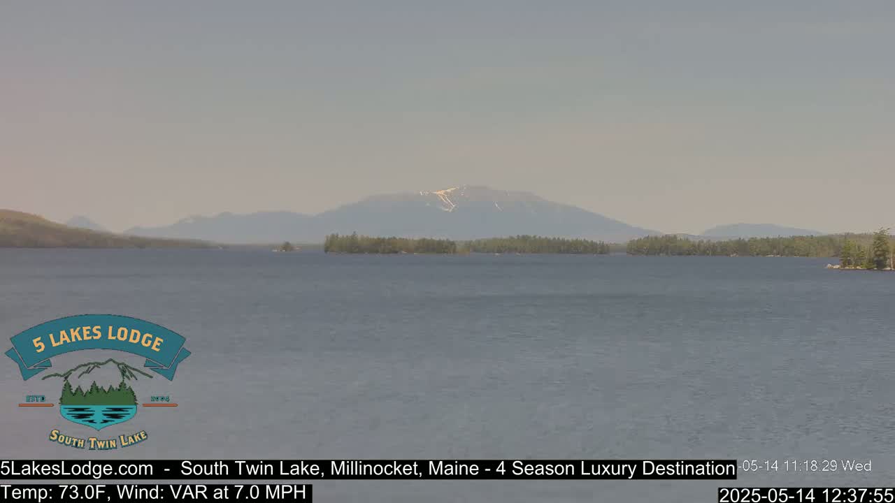 A calm lake with a mountain range in the background under a hazy sky.