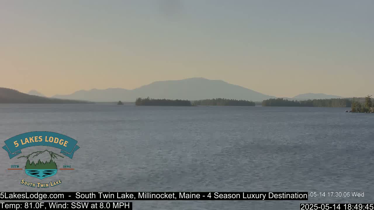 A calm lake with a distant mountain range under a pale, clear sky.