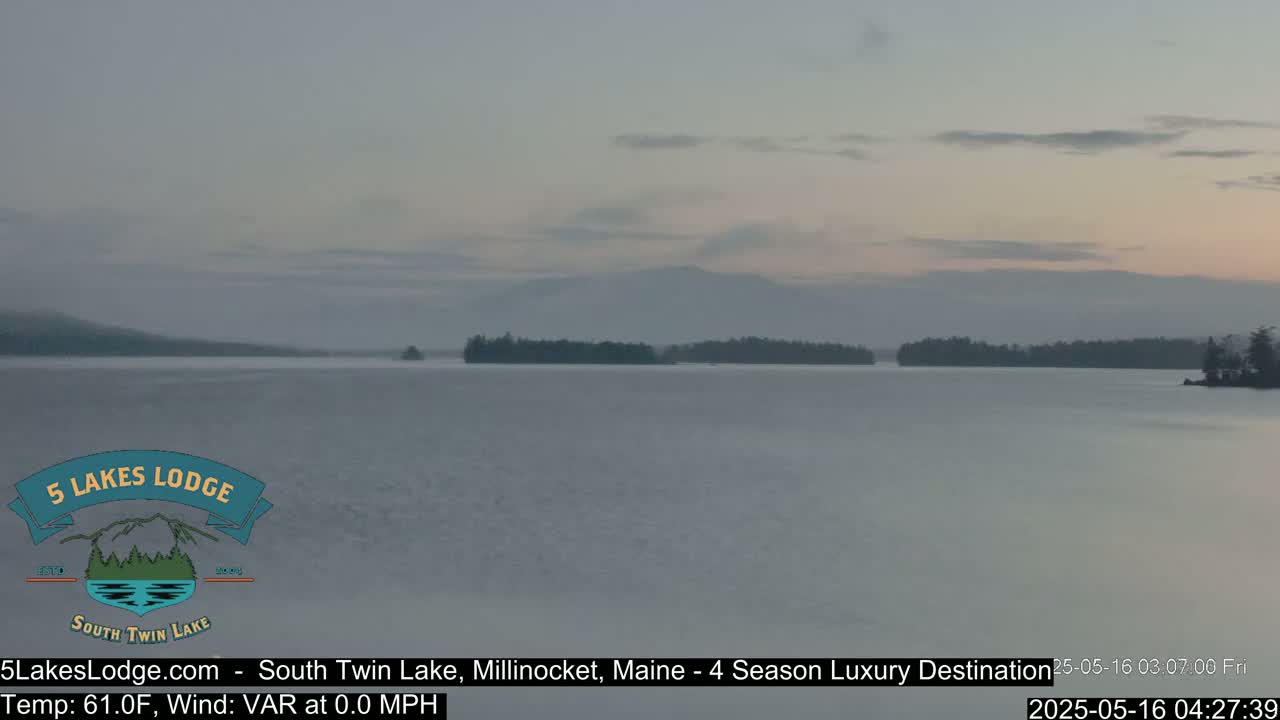 A calm lake at dawn, with a hazy sky and distant mountains.