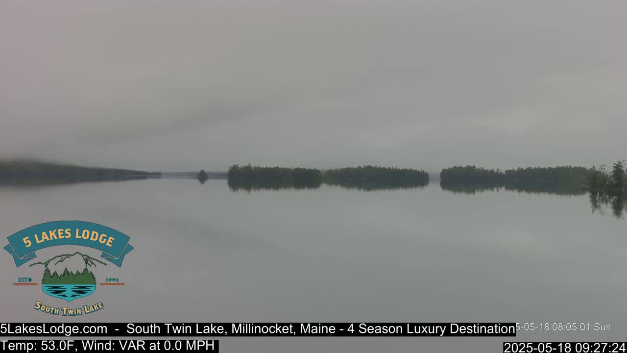 A calm lake with a hazy, foggy atmosphere shows a treeline across the middle, mirroring itself in the still water.