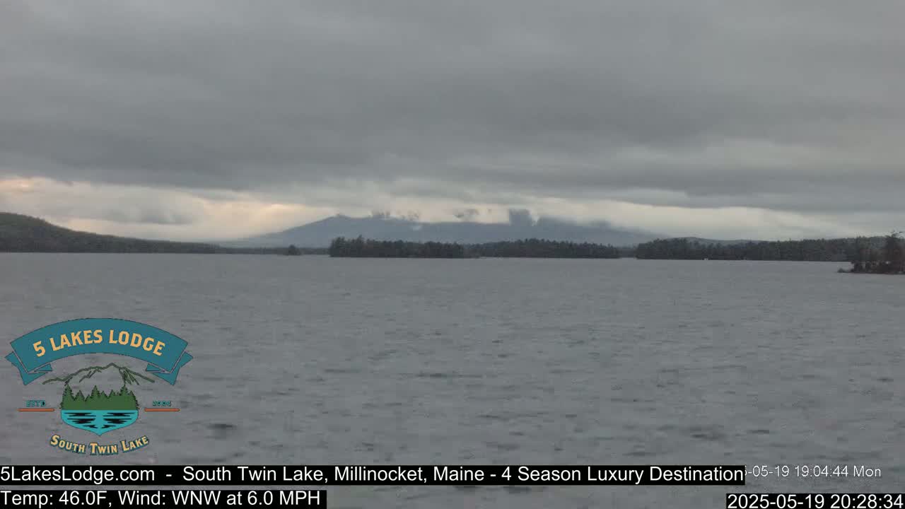 A calm lake under an overcast sky shows distant mountains.