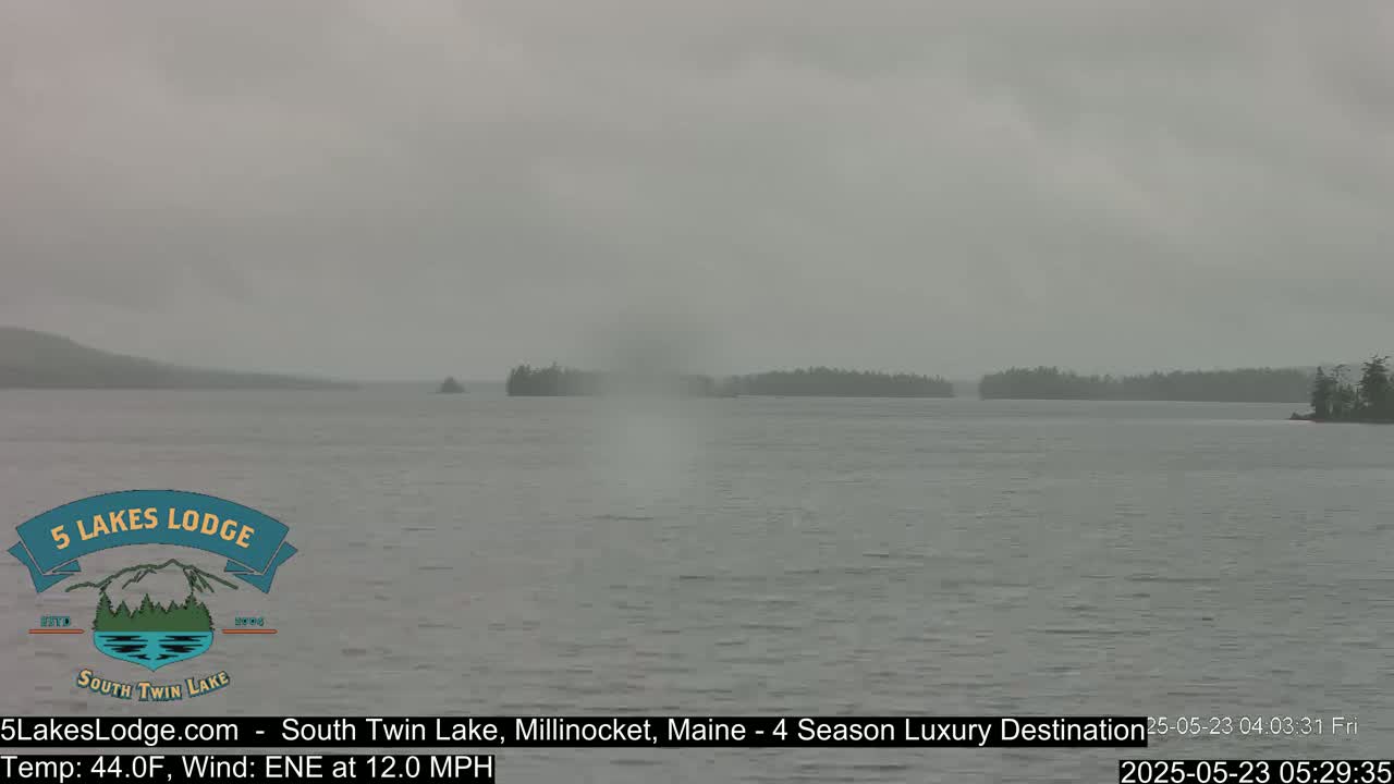 A hazy, gray day shows a calm lake with distant tree-covered land under an overcast sky.