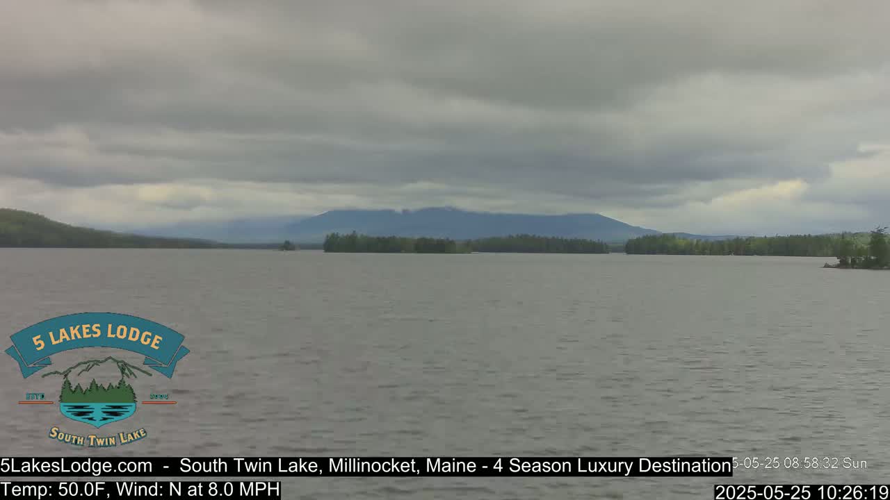 A calm lake under an overcast sky, with mountains in the background.