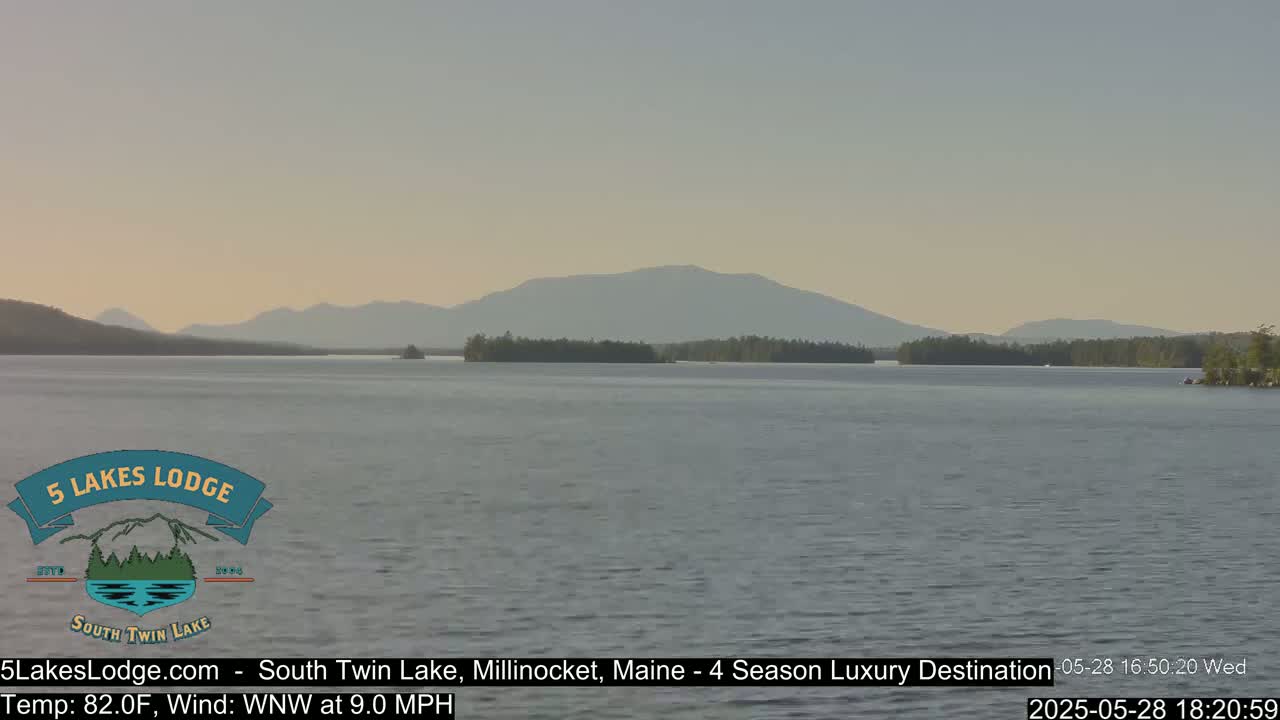 A calm lake stretches to distant mountains under a clear, light-grey sky.
