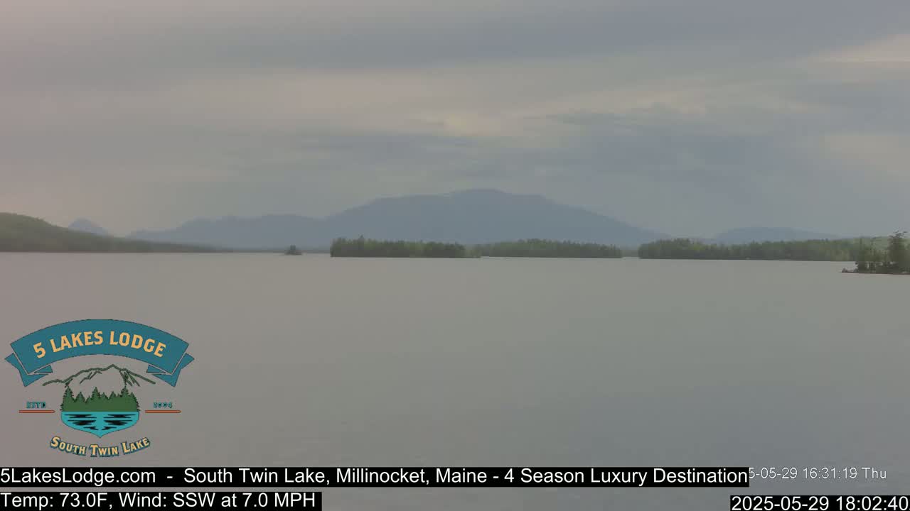 A calm lake stretches to distant, hazy mountains under an overcast sky.