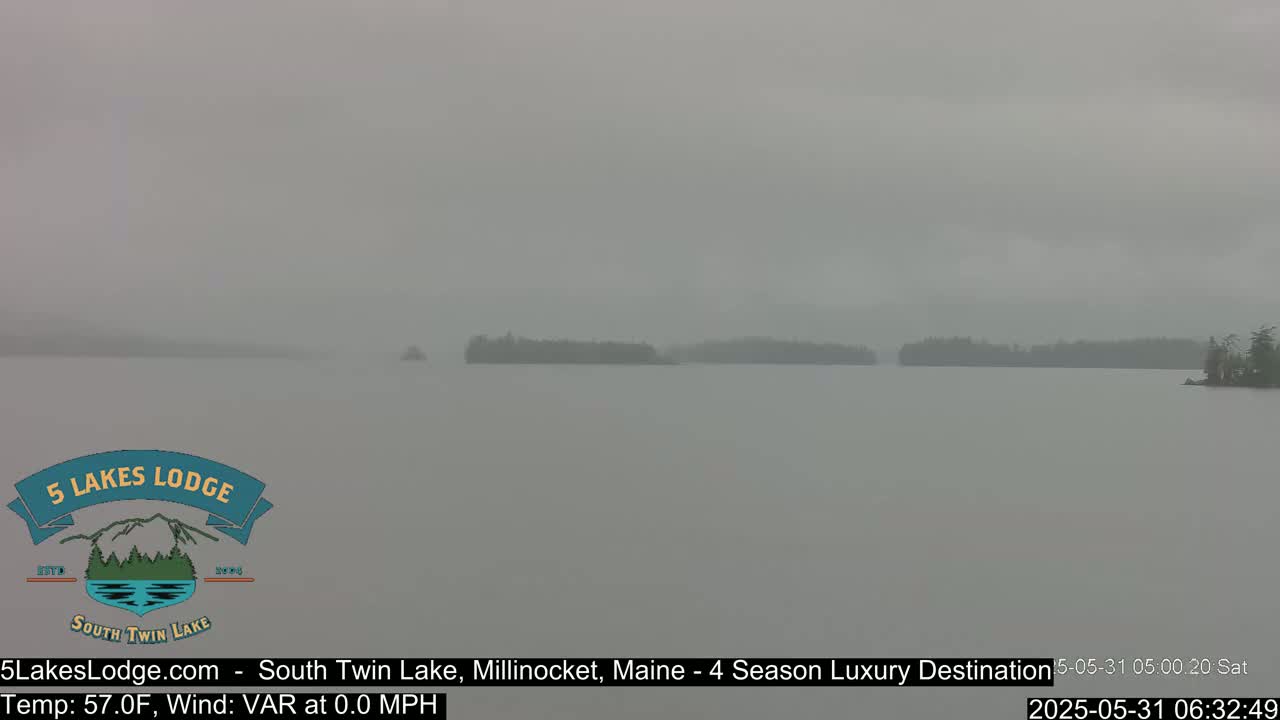 A foggy, calm lake is seen with a dark shoreline in the distance.