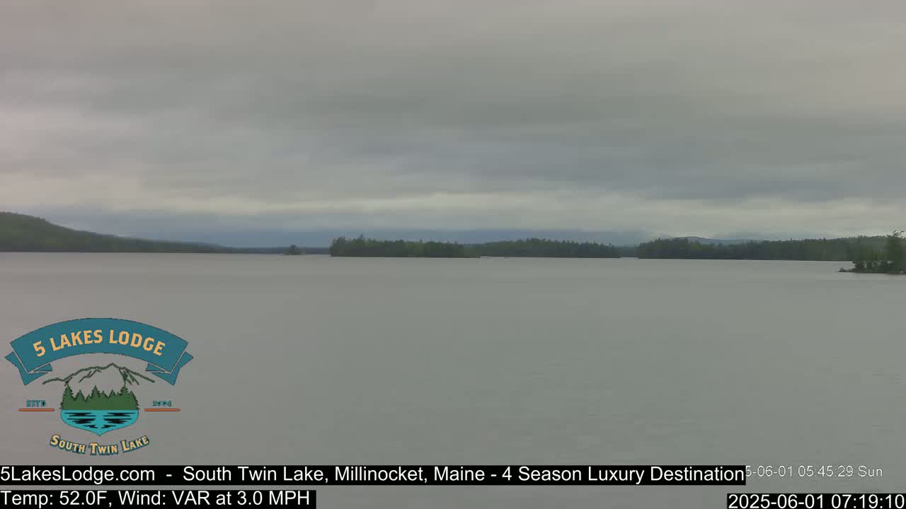 A calm lake under an overcast sky is surrounded by a treeline.