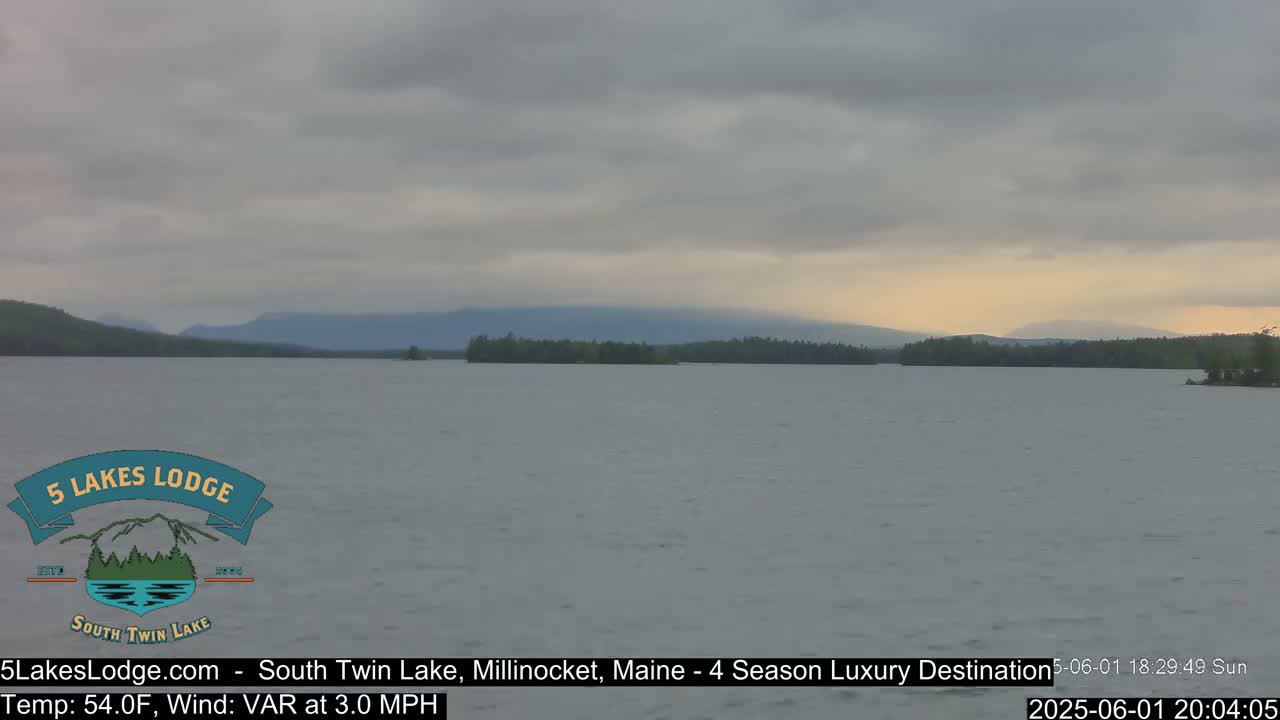 A calm lake with a distant mountain range under an overcast sky.