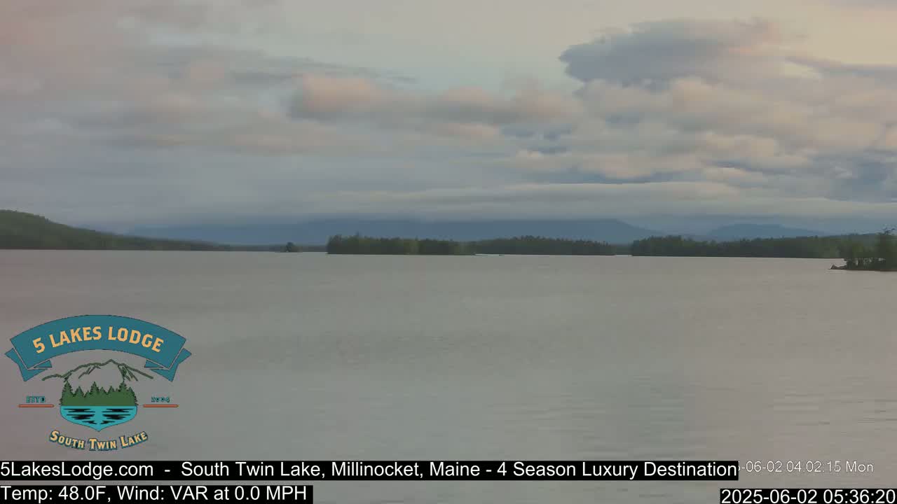 A calm lake is seen under a mostly cloudy sky.