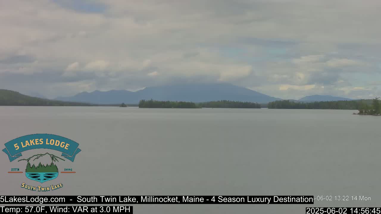 A calm lake with a mountain range in the background under a cloudy sky.