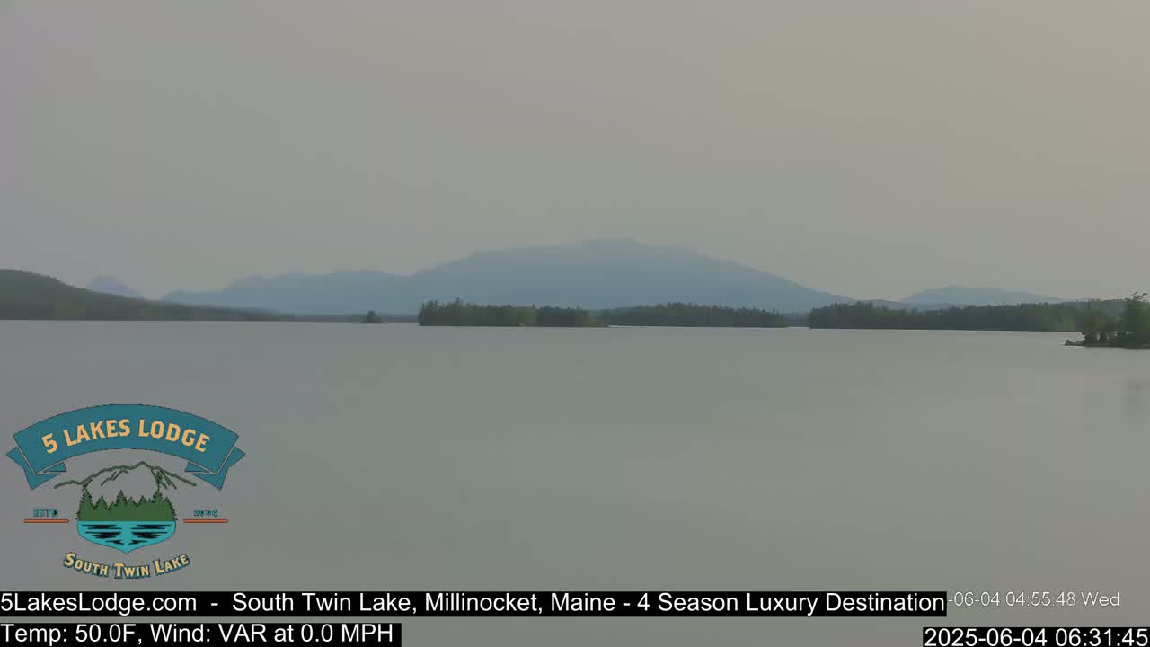 A hazy view of a calm lake with a distant mountain range under a muted sky.