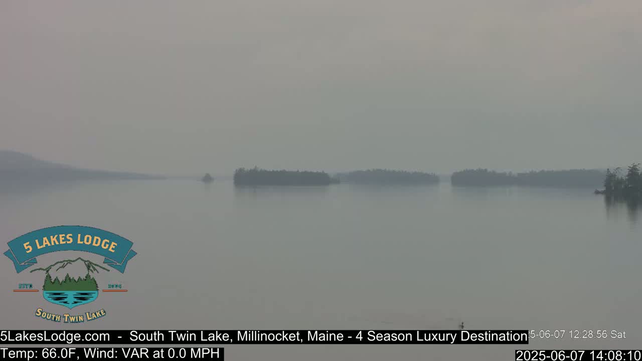 A hazy, calm lake is seen with several small, dark islands in the distance.