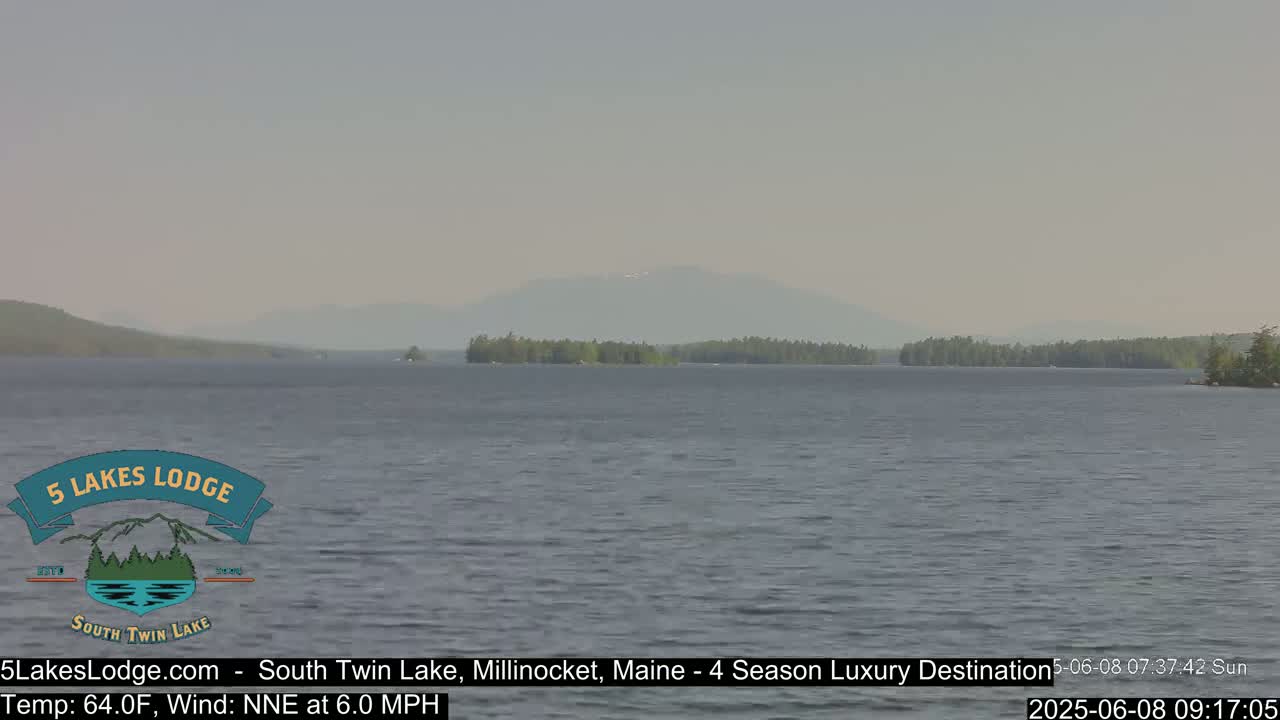 A calm lake with a distant mountain range under a hazy sky is visible, with a gentle north-northeast wind.