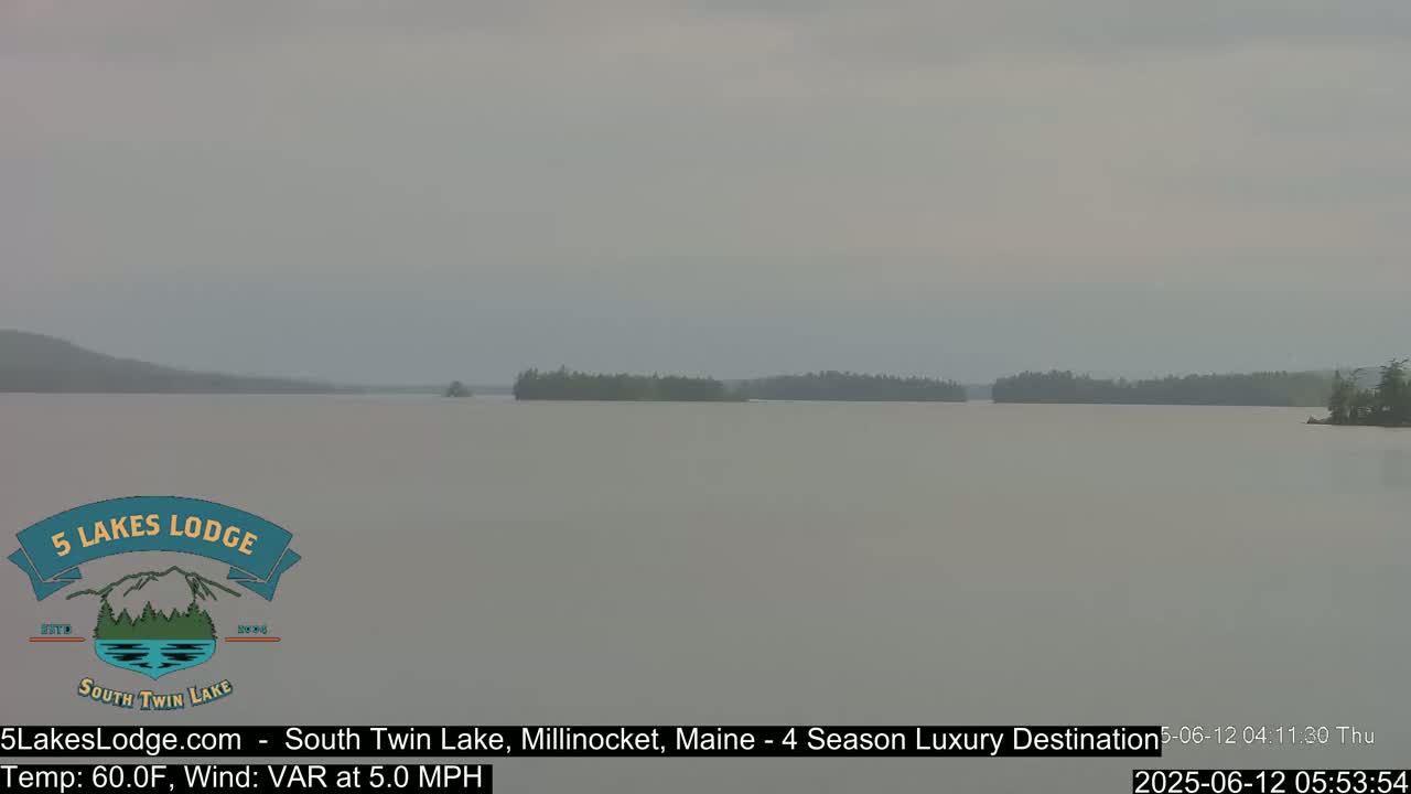 A hazy view of a calm lake with tree-lined shores in the distance.