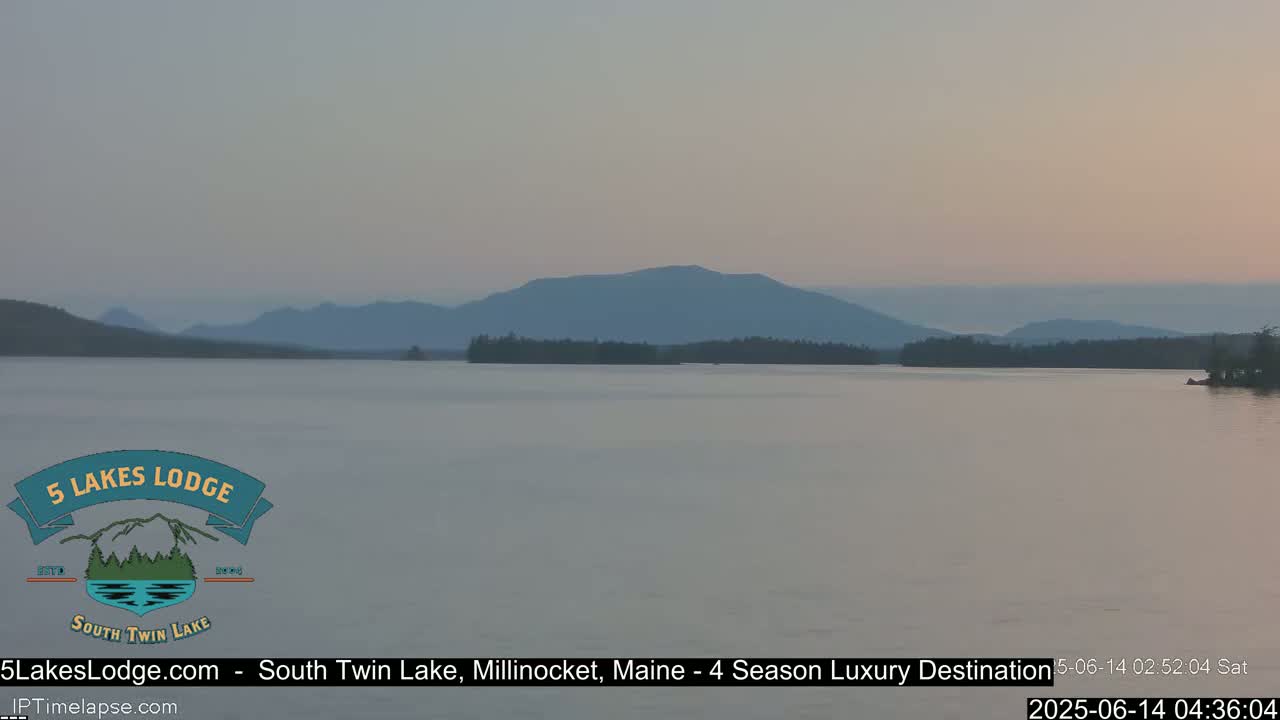 A calm lake stretches towards hazy mountains under a pale, dusky sky.