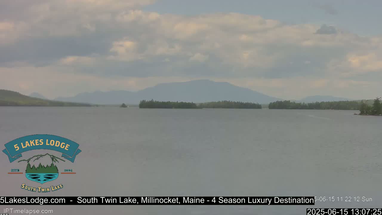 A calm lake with a distant mountain range under a partly cloudy sky.