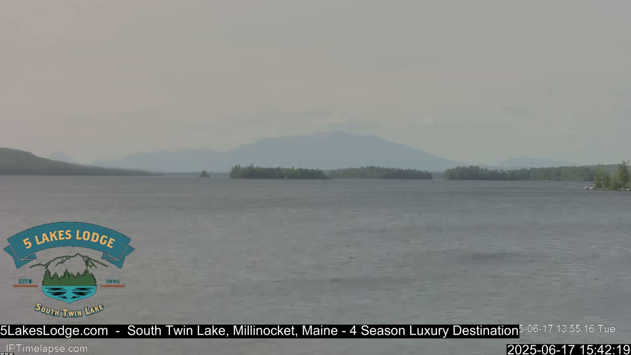 A calm lake with a hazy sky and distant mountains is visible under an overcast sky.