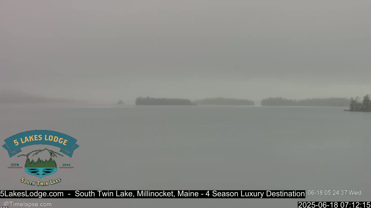 A hazy, overcast view shows a calm lake with indistinct tree-covered landmasses in the distance.