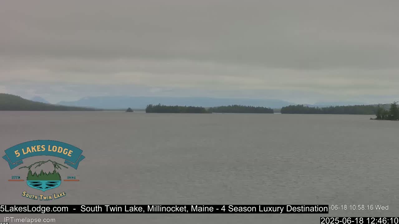 A calm lake stretches to distant, low-lying mountains under an overcast sky.