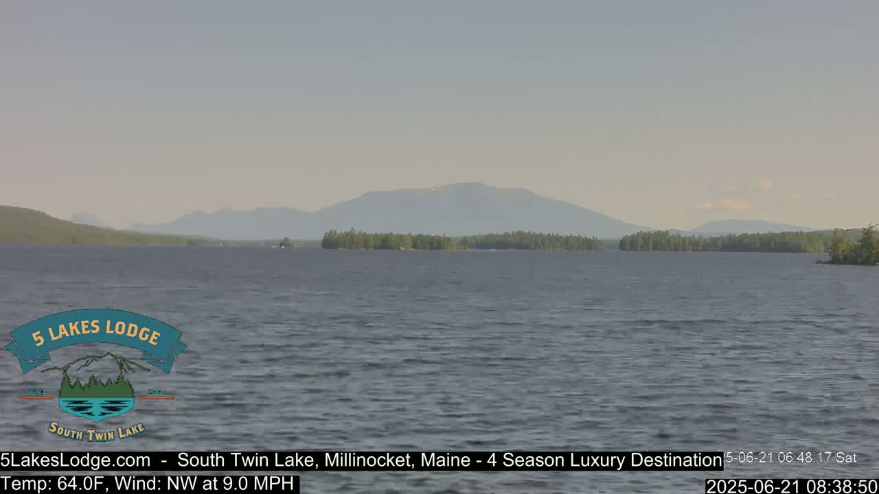 A calm lake with a distant mountain range under a hazy sky, with a light northwest wind.