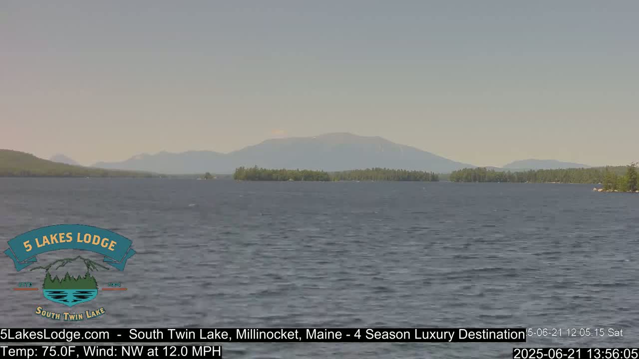 A calm lake with a distant mountain range under a hazy sky, with a northwest wind at 12 mph.