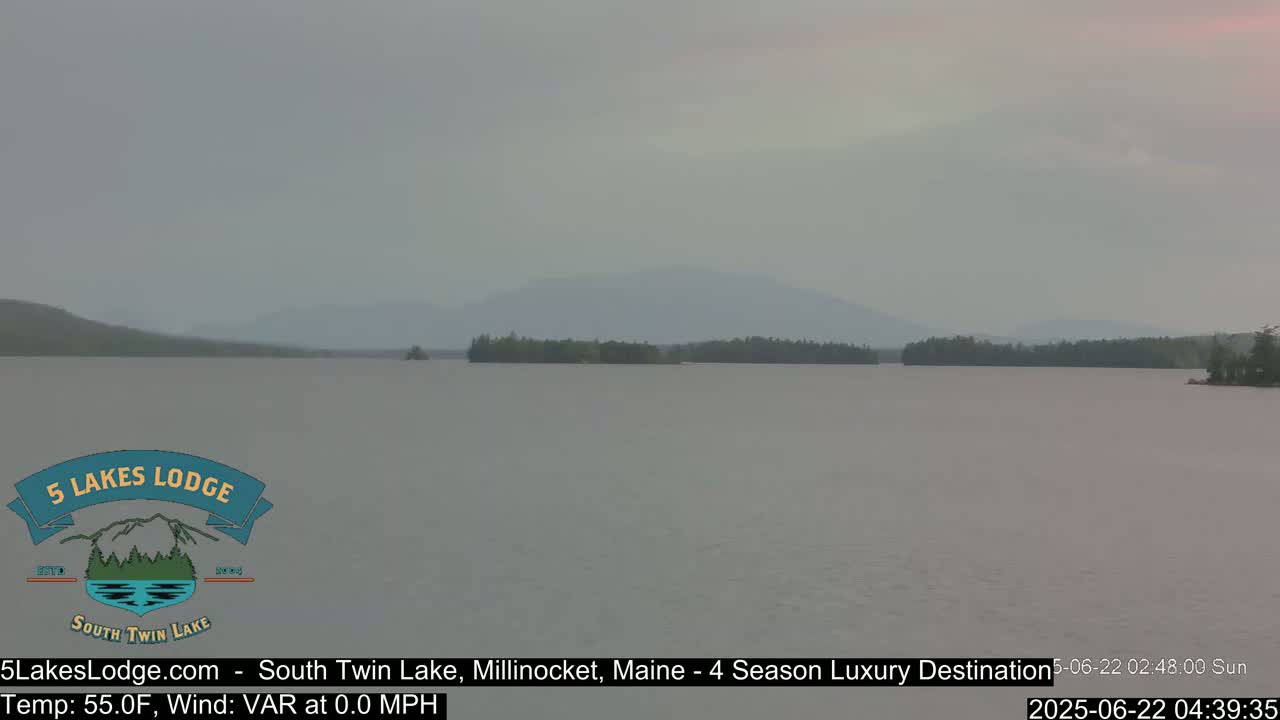 A calm lake with a distant mountain range is visible under an overcast sky.